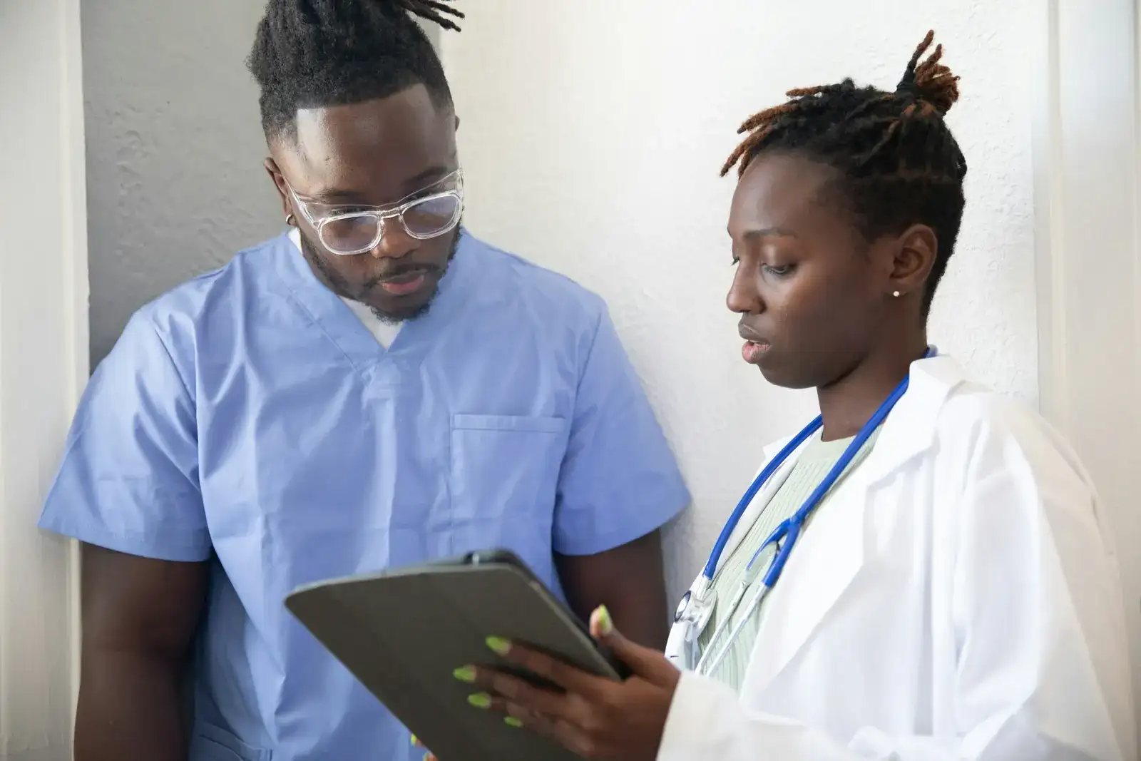 Two clinicians in scrubs and a white coat review a tablet computer together
