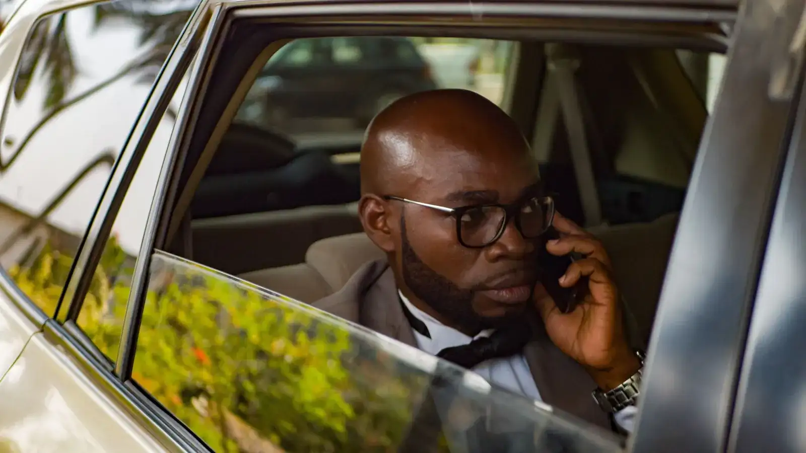 A businessman takes a phone call from the back seat of a car